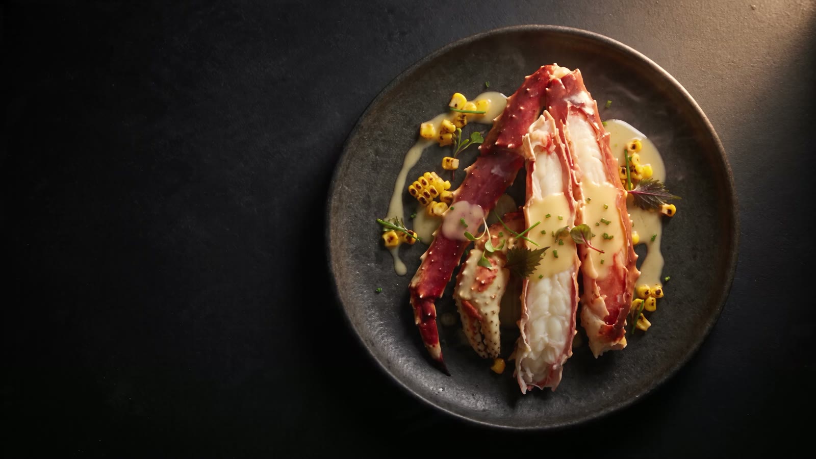 Split king crab legs napped in yuzu kosho beurre blanc with charred corn, steaming on dark ceramic